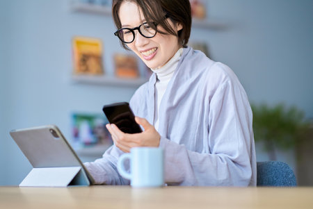 A woman operating a tablet PC and smartphone in the roomの写真素材