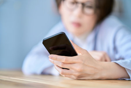 A woman operating a smartphone looking tired in the roomの写真素材