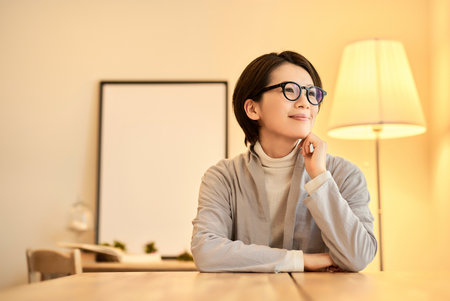A middle-aged woman with a relaxed expression in a room with warm indoor lightingの写真素材