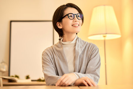 A middle-aged woman with a relaxed expression in a room with warm indoor lightingの写真素材