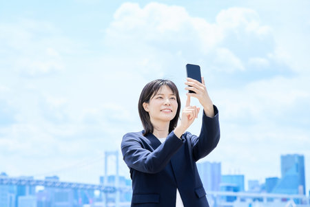 A young businesswoman operating a smartphone outdoorsの写真素材