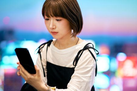 A young woman operating a smartphone and night viewの写真素材