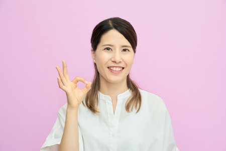A young woman making an OK hand sign indoorsの写真素材