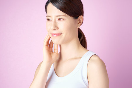 A woman checking her skin condition with a pink backgroundの写真素材
