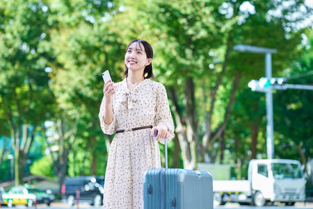 Young woman walking through the city with a suitcase and a smartphoneの写真素材