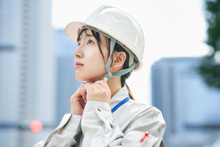 A young woman wearing work clothes and a helmet outdoors