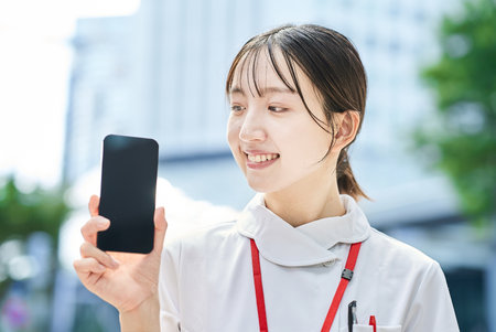 A young nurse holding a smartphone outdoorsの写真素材