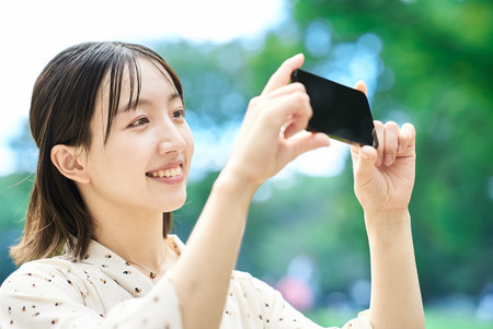 Young woman taking a picture with a smartphone outdoorsの写真素材