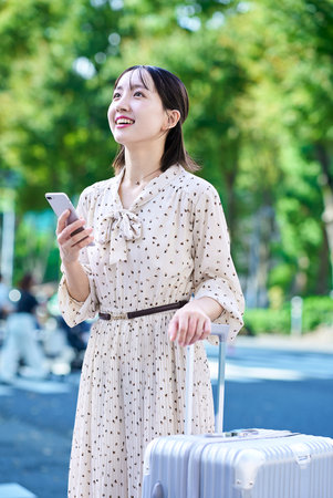 Young woman walking through the city with a suitcase and a smartphoneの写真素材