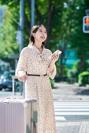 Young woman walking through the city with a suitcase and a smartphoneの写真素材