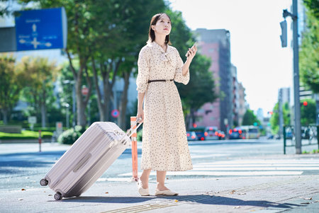 Young woman walking through the city with a suitcase and a smartphoneの写真素材