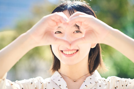 Young woman making a heart symbol hand sign outdoorsの写真素材