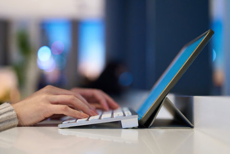 Hands typing on a computer keyboard in a space with a night view