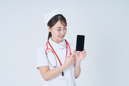 Female medical staff holding a smartphone and white backgroundの写真素材