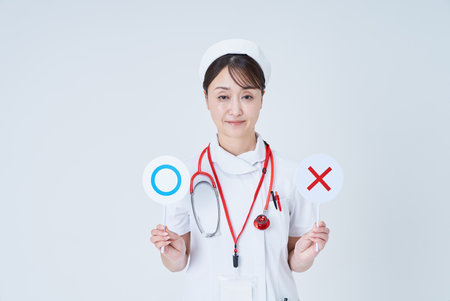 A woman in a white lab coat holding signs with marks written on them and a white backgroundの写真素材