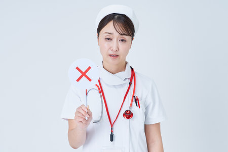 A woman in a white lab coat holding a sign with an X written on it and white backgroundの写真素材