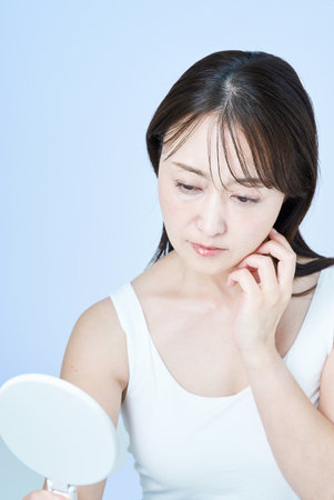 Middle-aged woman with a tired expression doing skin care and white backgroundの写真素材