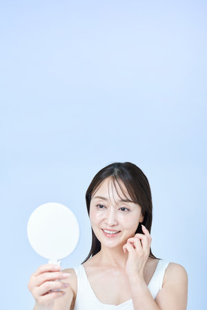Middle-aged woman looking at her face in the mirror and white backgroundの写真素材