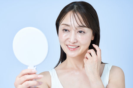 Middle-aged woman looking at her face in the mirror and white backgroundの写真素材