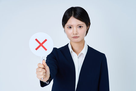 A woman in a suit holding a sign with a cross on it and white backgroundの写真素材