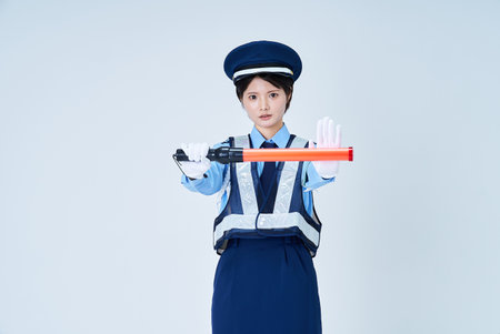 A woman wearing a security guard uniform and holding a red stick and white backgroundの写真素材