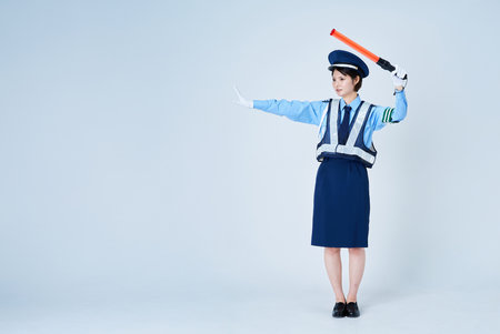 A woman wearing a security guard uniform and holding a red stick and white backgroundの写真素材