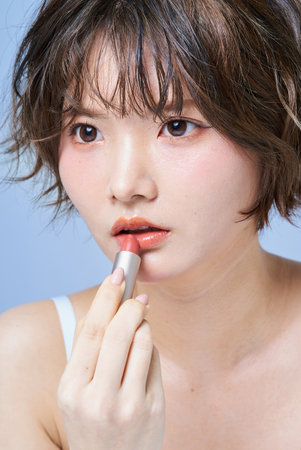 Young woman putting on make-up and white backgroundの写真素材