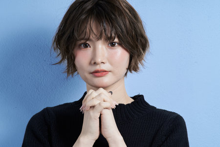 A young woman with short hair and a praying expression and white backgroundの写真素材