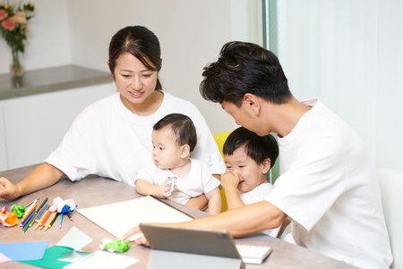 A father operating a computer in the living room while his family plays nearbyの写真素材