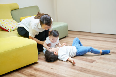 A mother and her children playing happily in a room with a sofaの写真素材