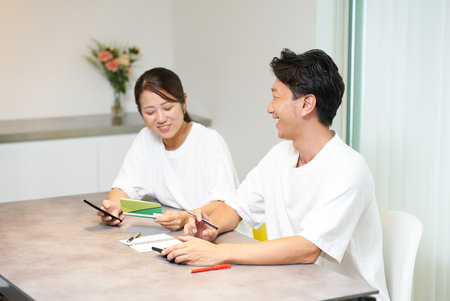 A man and a woman looking at their bank account passbook in the living roomの写真素材