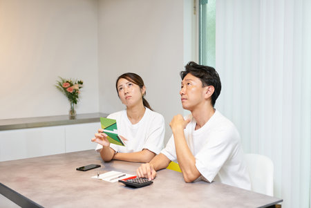 A man and a woman are thinking deeply about their bankbook in the living roomの写真素材