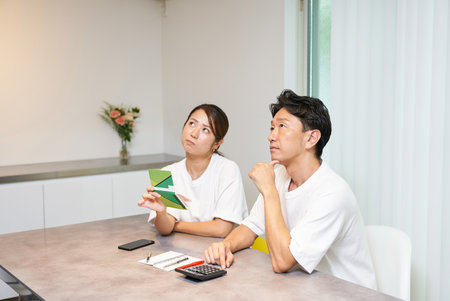 A man and a woman are thinking deeply about their bankbook in the living roomの写真素材