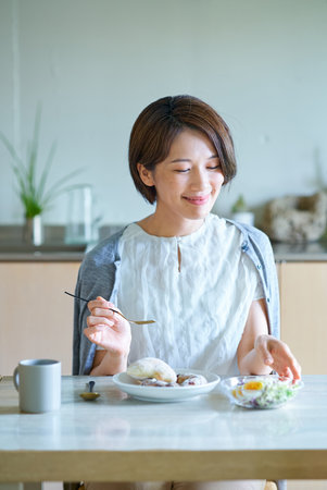 A middle-aged woman eating breakfast in her roomの写真素材