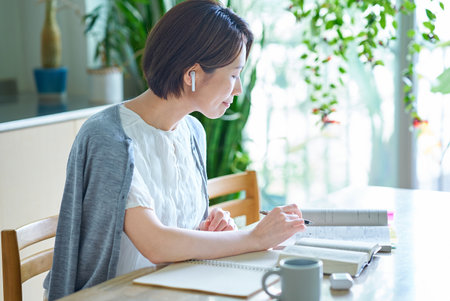 A woman studying in her room with earphonesの写真素材