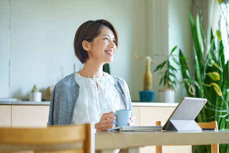 A woman taking a break with a mug while working indoorsの写真素材