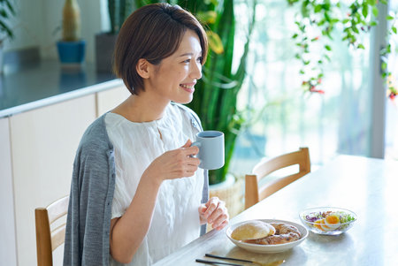 A middle-aged woman eating breakfast in her roomの写真素材