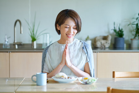 A middle-aged woman eating breakfast in her roomの写真素材