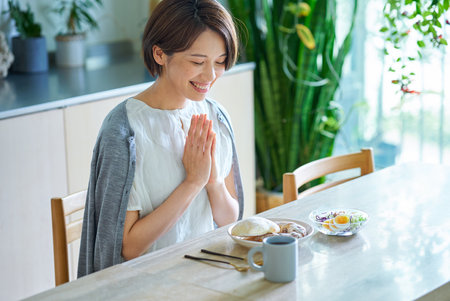 A middle-aged woman eating breakfast in her roomの写真素材