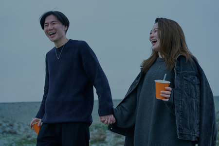 Young man and woman walking through sand dunes on a cloudy eveningの写真素材