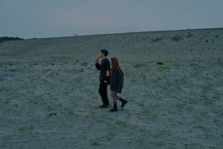 Young man and woman walking through sand dunes on a cloudy eveningの写真素材