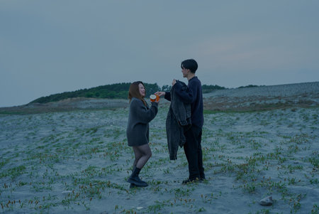 Young man and woman walking through sand dunes on a cloudy eveningの写真素材