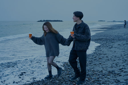 Young man and woman walking on the beach just after sunsetの写真素材