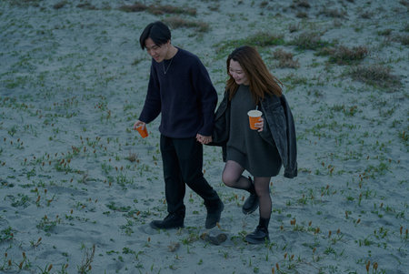 Young man and woman walking through sand dunes on a cloudy eveningの写真素材