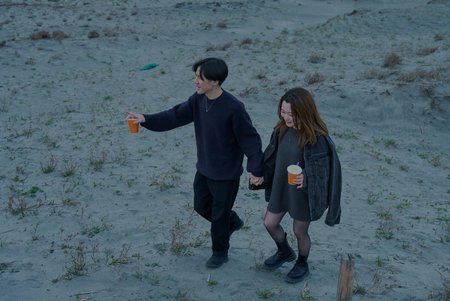 Young man and woman walking through sand dunes on a cloudy eveningの写真素材