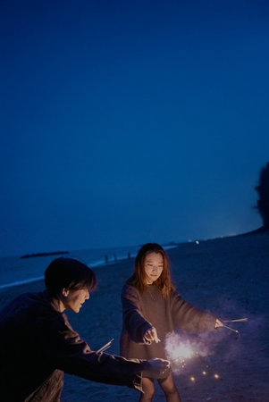 Young man and woman playing hand-held fireworks on the beach at nightの写真素材