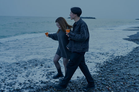 Young man and woman walking on the beach just after sunsetの写真素材