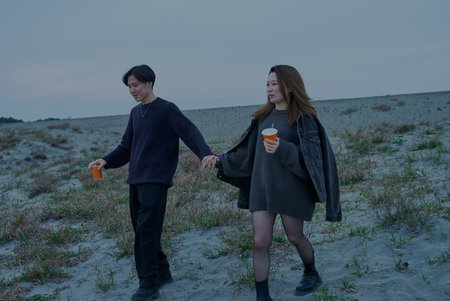 Young man and woman walking through sand dunes on a cloudy eveningの写真素材