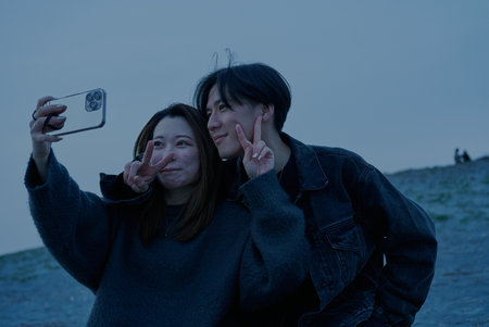 Young man and woman taking photos on the beach just after sunsetの写真素材