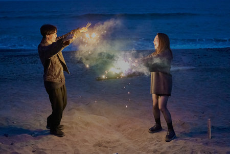 Young man and woman playing hand-held fireworks on the beach at nightの写真素材
